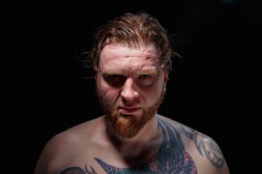 Siyah arka planda gözleri kapalı dövmeli bir adamın fotoğrafı.