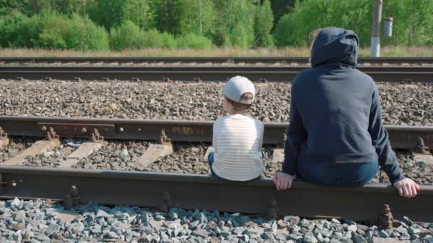 Tiro de menina e menino sentado em trilhos — Vídeo de Stock