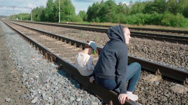 女孩和男孩坐在铁轨上的镜头 — 图库视频影像