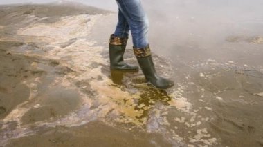 Kum kıyısında lastik botlarla yürüyen bir adamın görüntüsü.