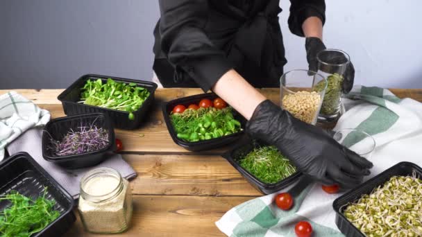 Filmagem de mulher em luvas pretas salada de cozinha com micro verde — Vídeo de Stock