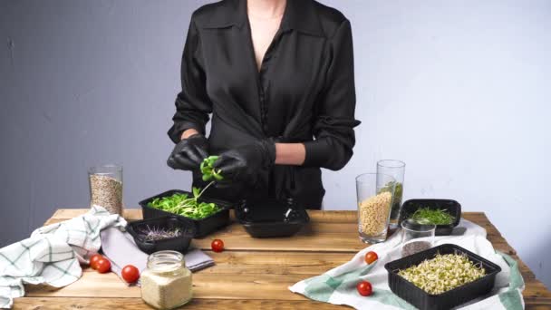 Filmagem de mulher em luvas pretas salada de cozinha com micro verde e sementes — Vídeo de Stock