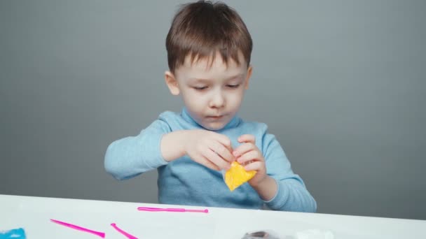 Filmación de un niño de cuatro años esculpido en plastilina sobre fondo gris — Vídeos de Stock