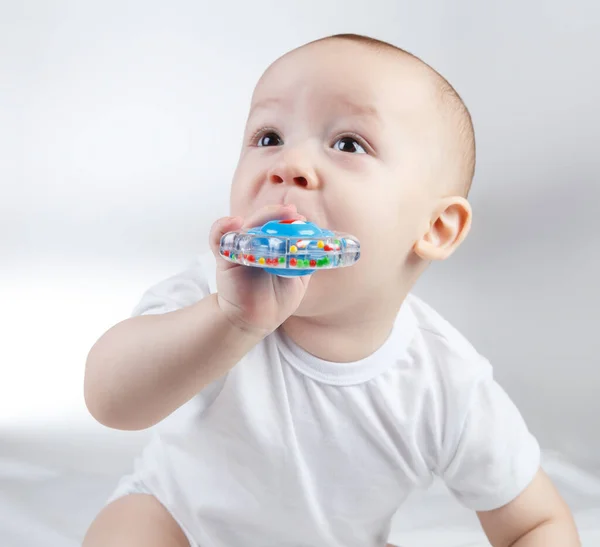 Foto de um bebê de dez meses com chocalho azul na boca — Fotografia de Stock