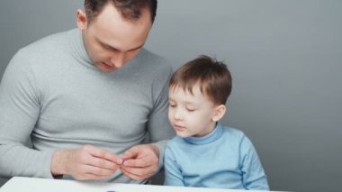 Baba ve oğul, gri arka planda plastikten hayvan heykeli yapıyorlar.