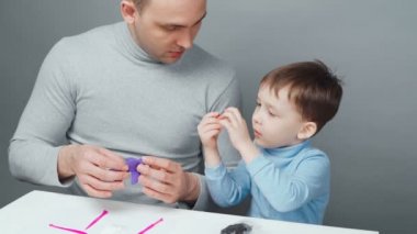 Baba ve oğlunun gri arka planda plastikinden hayvan yapmaları.