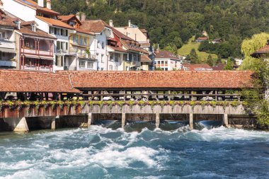 Thun 'daki eski tarihi ahşap köprü Aare nehri üzerinde turkuaz su, dağlık şehir manzarası. İsviçre