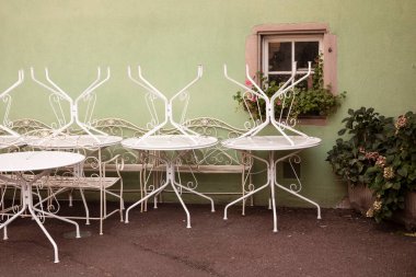 Kapalı restoranda klasik beyaz masalar baş aşağı duruyor. Romantik pencereli yeşil duvar ve yeşil bitkiler. Eski Fransız şehrinin büyüleyici caddesi. Colmar, Fransa. Geleneksel Fransız Kafe Bahçesi.