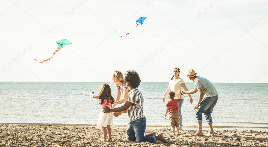 Group of happy families with parent and children playing with kite at beach vacation - Summer joy carefree concept with mixed race people having fun together at sunset  - Bright vintage  filter