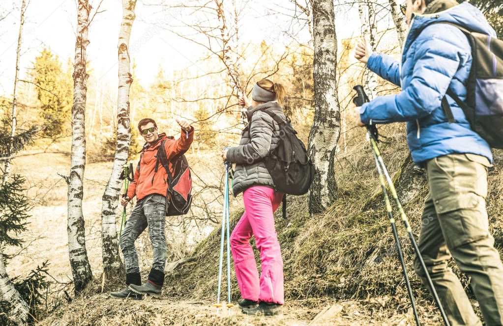 Friends group trekking in forest on french alps at sunset - Hikers with backpacks and sticks walking on mountain woods - Wanderlust travel concept with young people at excursion - Focus on left guy