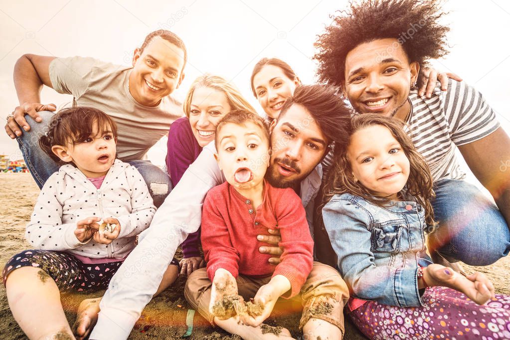 Happy multiracial families taking selfie at beach making funny faces - Multicultural happiness joy and love concept with mixed race people having fun outdoor at sunset - Bright pastel backlight filter