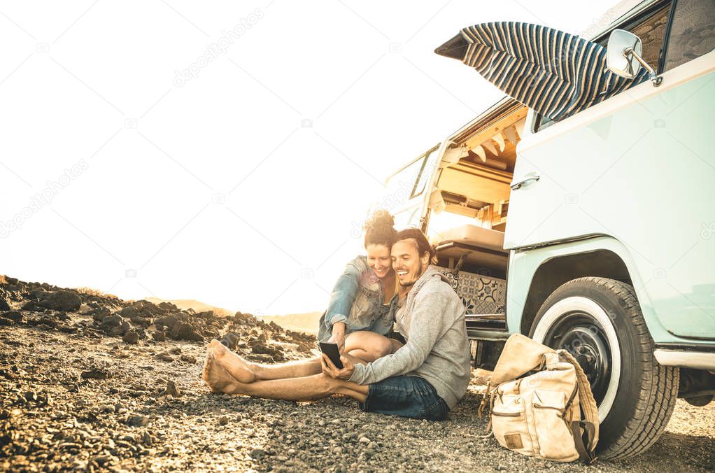 Hipster couple traveling together on oldtimer mini van transport - Travel lifestyle concept with indie people on minivan adventure trip having fun with mobile smart phone - Warm desaturated filter