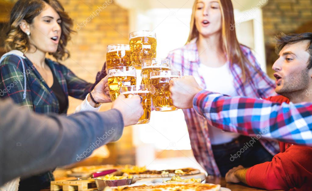 Happy friends group drinking beer and eating pizza at bar restaurant - Friendship concept with young people having fun together at risto pub pizzeria - Focus on middle pint glass - Vivid warm filter