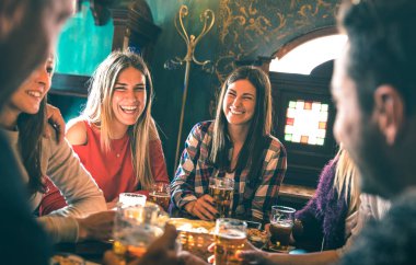 Group of happy friends drinking beer at brewery bar restaurant - Friendship concept with young millenial people enjoying time together having fun vintage pub - Focus right woman - High iso image clipart