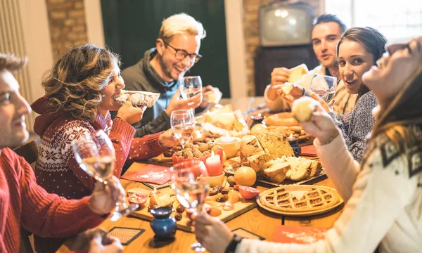 Vooraanzicht van de groep vrienden proeverij kerst snoepjes eten en plezier thuis drinken champagne mousserende wijn - Winter vakantie concept met mensen die genieten van tijd samen eten - Warm filter — Stockfoto