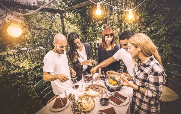 Felices amigos divirtiéndose comiendo comida local en el festival del jardín - Concepto de amistad y vacaciones con la gente junta en la bodega de viñedos de granja - Filtro vintage cálido con iluminación eléctrica artificial —  Fotos de Stock