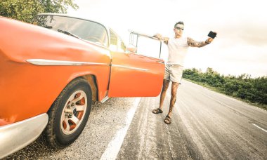 Genç hippi selfie eski model araba ile yolculuk sırasında Küba - her zaman sosyal medya etkileyen yaşam tarzına bağlı seyahat yolculuk tutkusu kavramı - parlak retro filtrede alarak dövmeli adam moda
