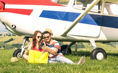 Young couple of lovers having a rest during charter airplane excursion - Wanderlust concept of alternative people lifestyle traveling around the world - Love and fun sharing images on mobile phone clipart