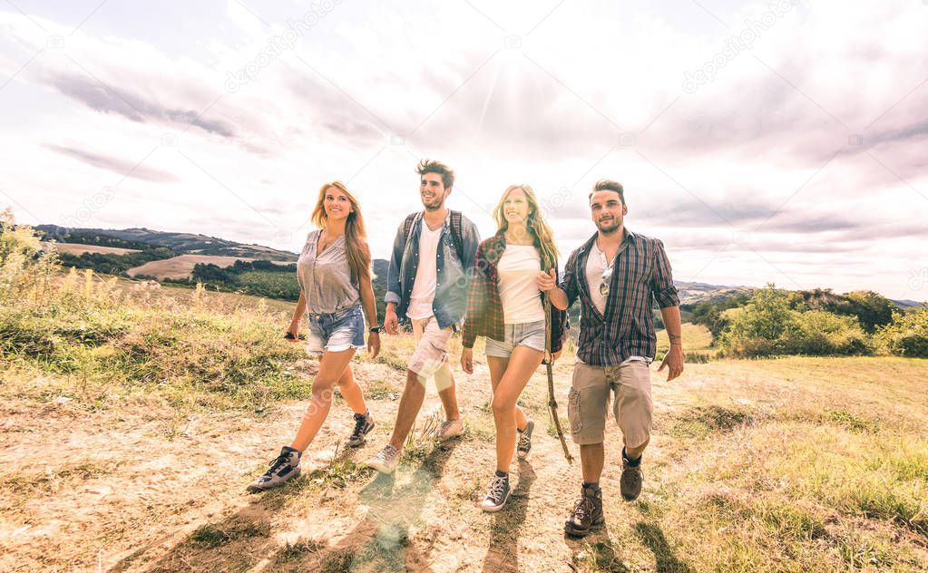 Best friends group walking free on grass meadow - Friendship and freedom concept with young millenial people sharing camping experience - Vintage desaturated filter with backlight contrast sunshine