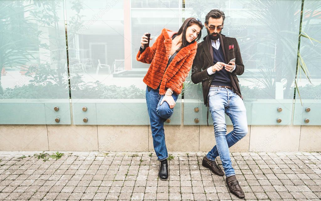 Happy hipster couple having fun with mobile smart phone at outdoors location - Friendship concept with best friends connecting and sharing content on social media - Millennial generation dating online