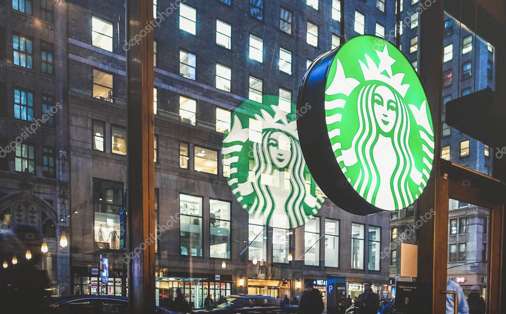 NEW YORK - MARCH 25, 2015: Starbucks sign at cafe shop by night with glass reflections on Nyc nightscape - The enterprise is an american coffee company and coffeehouse chain founded in 1971
