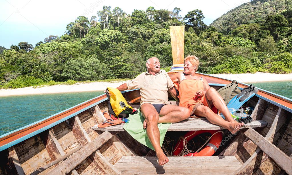 Senior couple vacationer relaxing at island hopping tour after beach exploration during snorkel boat trip in Thailand - Active elderly and travel concept on tour around world - Warm day bright filter