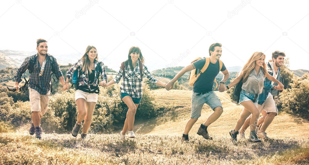 Group of friends running on grass meadow on country side - Happy friendship and freedom concept with young millenial people moving free at camping experience - Vintage desaturated filter