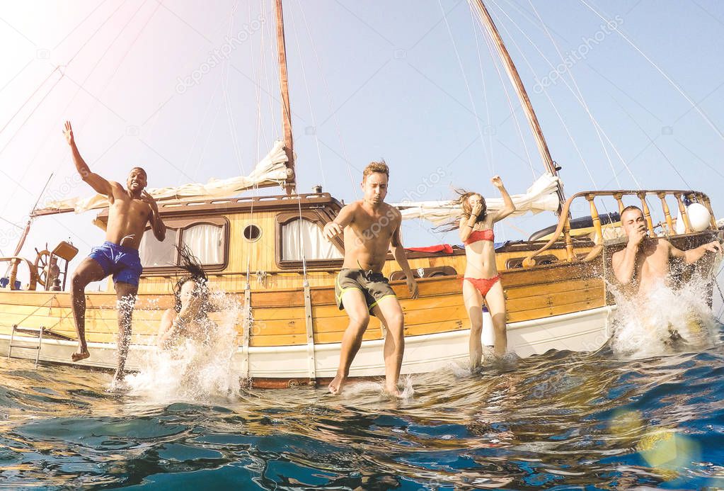 Frontal view of young millennial friends jumping from sailboat on sea ocean trip - Rich guys and girls having fun together in summer boat party day - Exclusive vacation concept on warm bright filter