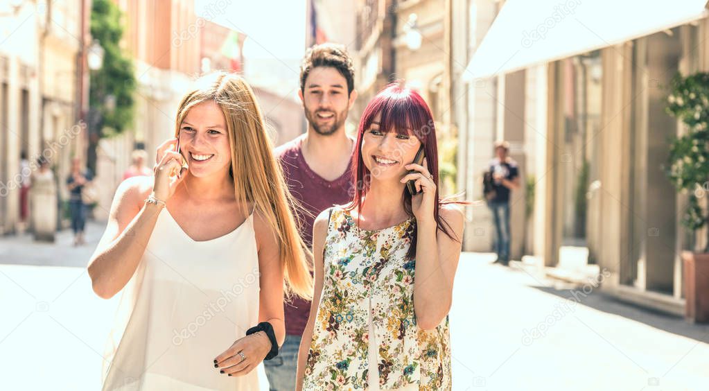 Young man following pretty women while having fun together on city street - Technology concept in everyday lifestyle with millenials people talking and using mobile smart phone - Bright filter
