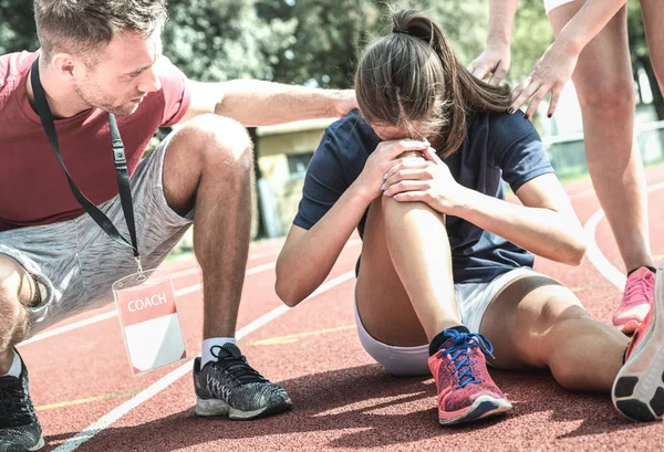 Female athlete getting injured during athletic run training - Male coach taking care on sport pupil after physical accident - Team care concept with young sporty people facing mishaps casualty — Stock Photo, Image