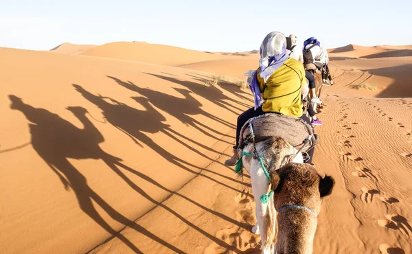 Turistas caravana montando dromedários através de dunas de areia no deserto do Saara perto de Merzuga em Marrocos - conceito de viagem Wanderlust com as pessoas viajantes em passeio de aventura viagem de camelo - filtro brilhante quente — Fotografia de Stock