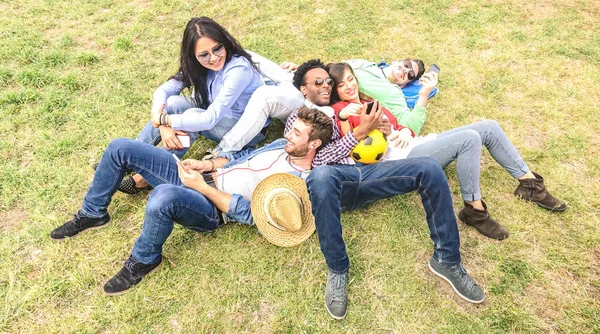 牧草地ピクニックで楽しんでいる多民族の親友 - 春の夏の時間に携帯電話と一緒に時間を共有する若者ミレニアルとの幸せな友情の楽しいコンセプト - 明るい午後のフィルタ — ストック写真