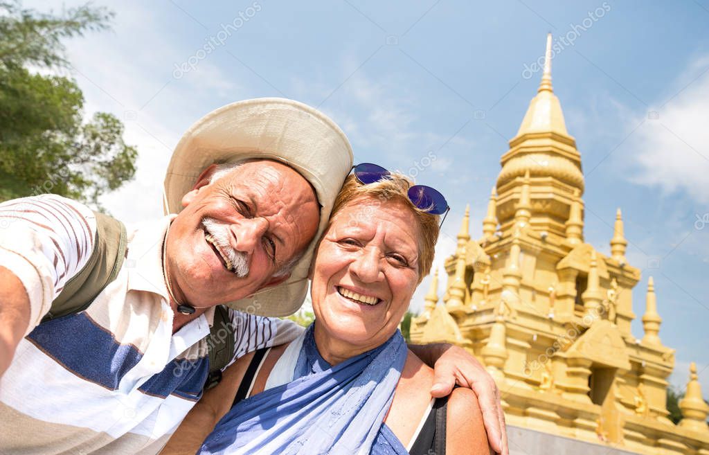 Senior couple taking selfie at golden temple in Ko Samui - Happy retired people traveling to Thailand wonders - Active elderly concept and fun around the world to south east asia destinations