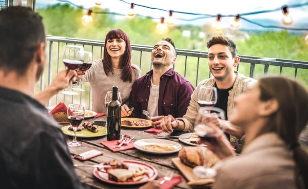 Jovens amigos se divertindo bebendo vinho tinto na varanda penthouse jantar - Pessoas felizes comendo comida bbq em restaurante alternativo fantasia juntos - Dinning lifestyle concept on warm vintage filter — Fotografia de Stock