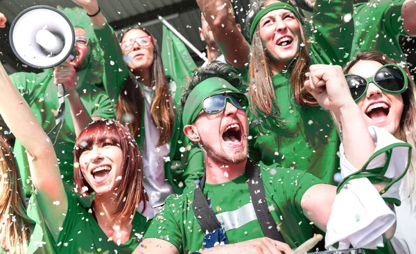 Jóvenes aficionados aficionados al fútbol aplaudiendo con confeti viendo partido de copa de fútbol local en el estadio - Amigos grupo de personas en camisetas verdes que se divierten en la final del campeonato mundial de deporte —  Fotos de Stock