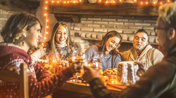Happy friends tasting christmas sweet food at home fun party - New year's eve mood with white wine glasses toast - Winter holiday concept with young people eating together - Bulb lights warm filter
