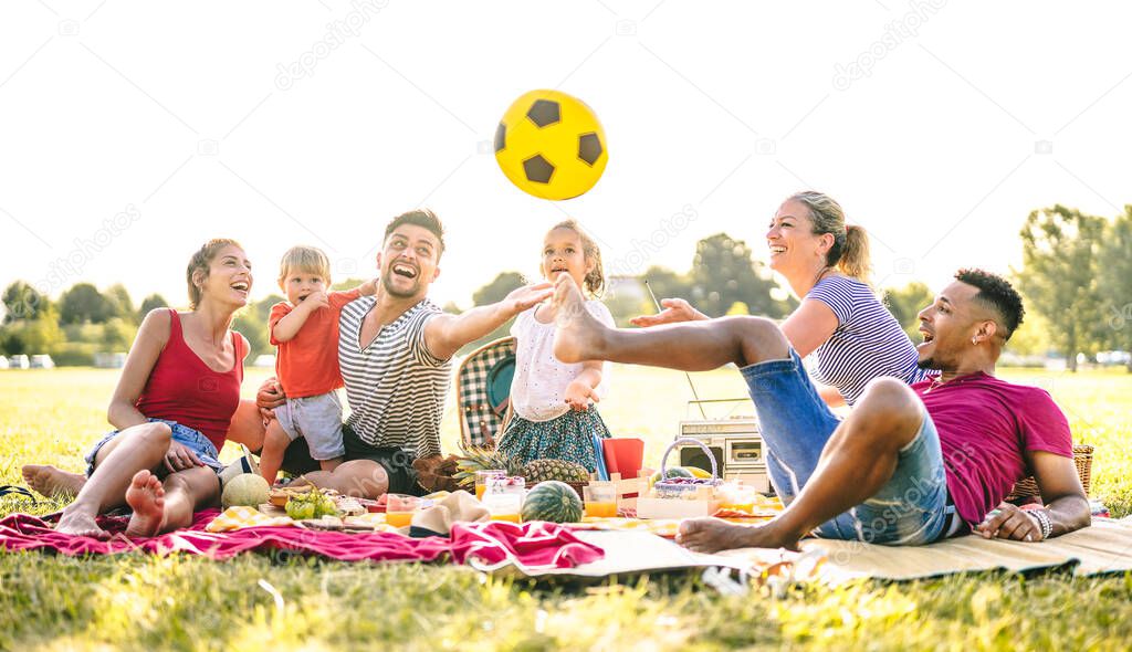 Happy multiracial families having fun with cute kids at pic nic garden party - Multicultural joy and love concept with mixed race people playing together with children at park - Bright sunny filter