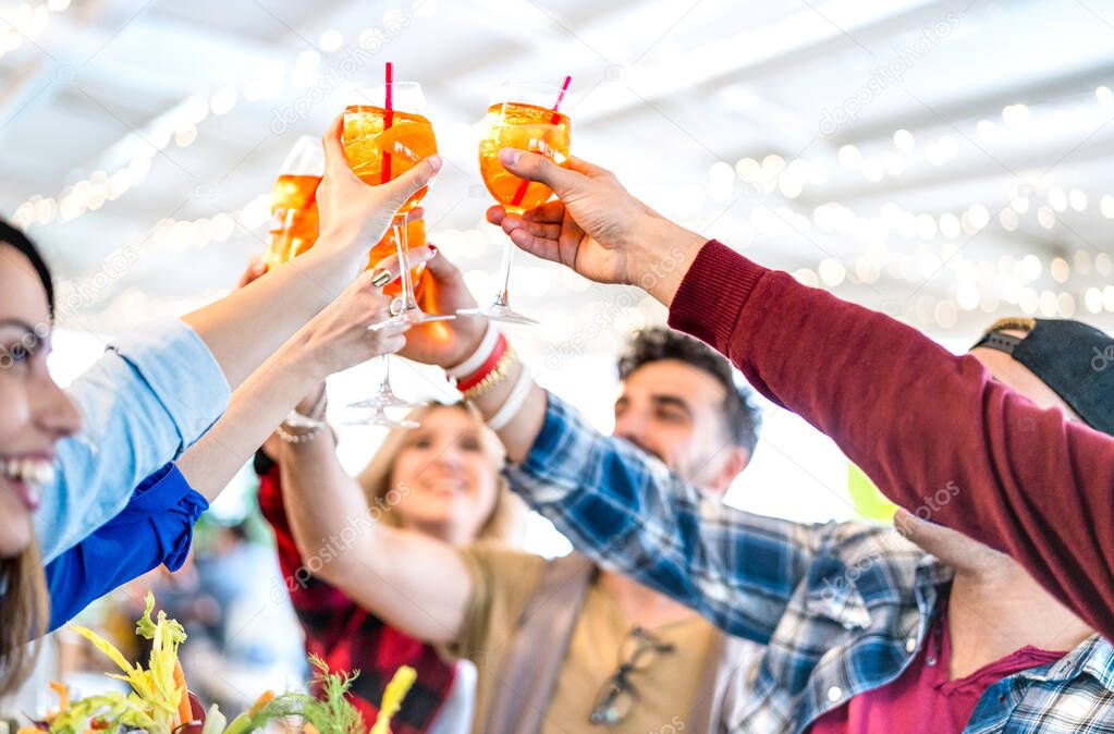 People toasting spritz drink at fashion cocktail bar restaurant - Lifestyle concept with young friends having fun together drinking on happy hour at pub - Focus on orange glasses - Bright vivid filter