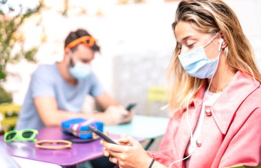 Kulaklıklı genç bir kadın cep telefonunda takip uygulaması kullanıyor - Yeni normal günlük yaşam tarzı kavramı sosyal medya platformlarında içerik paylaşımı - kız odaklı parlak filtre