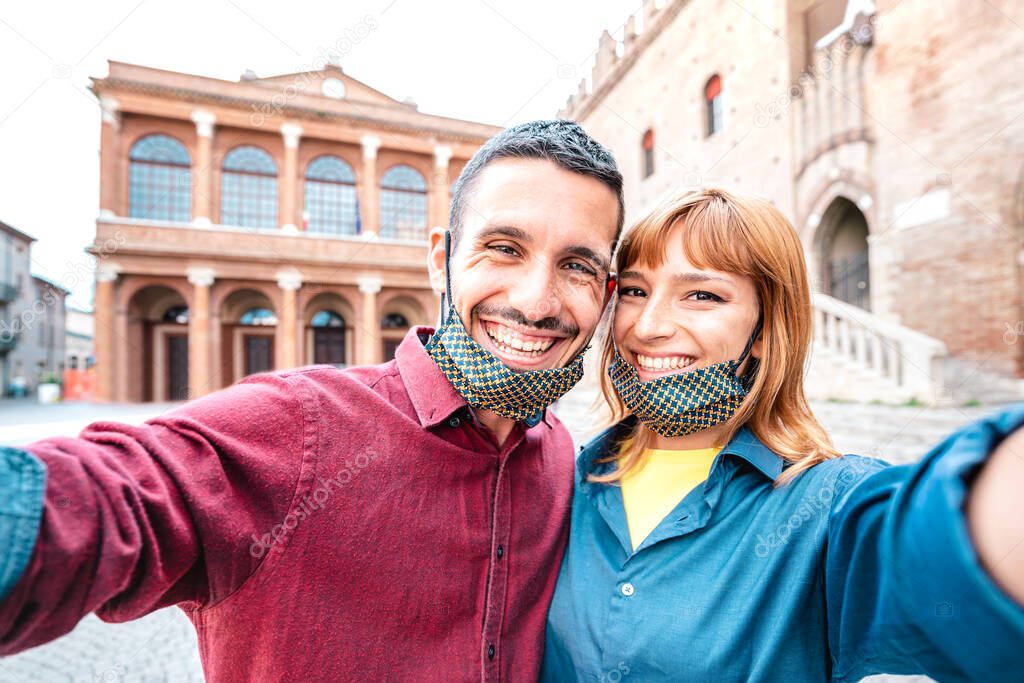 Happy boyfriend and girlfriend in love taking selfie with face masks at old town tour - Wanderlust life style travel concept with tourist couple on city sightseeing vacation - Bright warm filter
