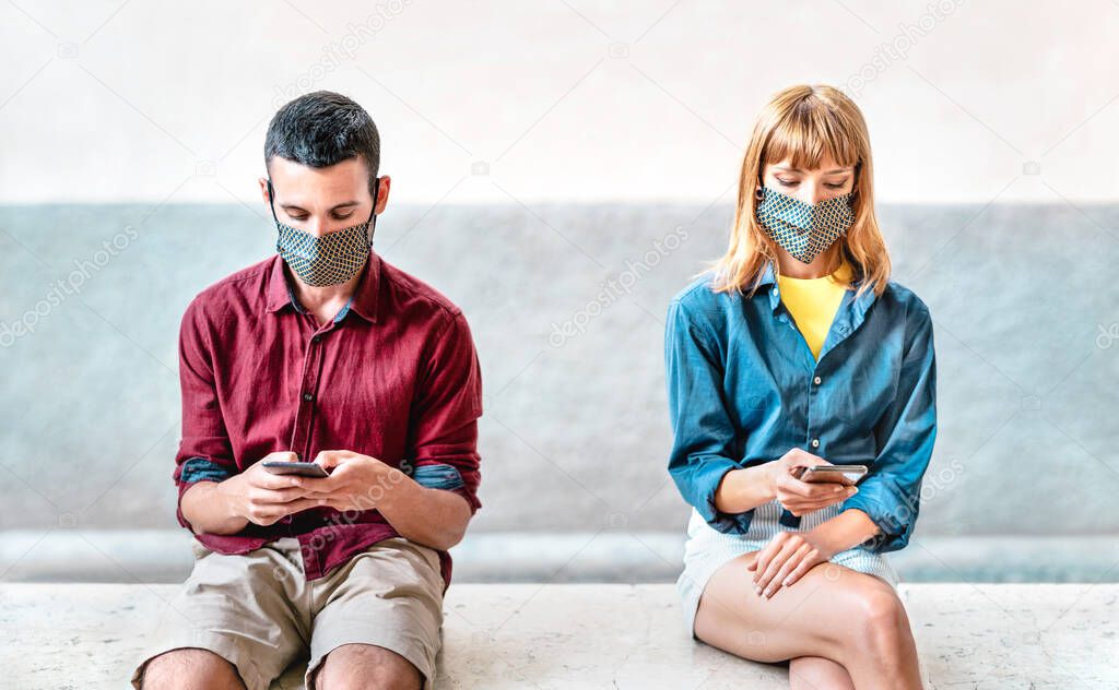 Bored addicted couple with protective masks using tracking app with mobile smartphones - Young millenial man and woman sharing content on social media - New normal lifestyle concept - Focus on faces