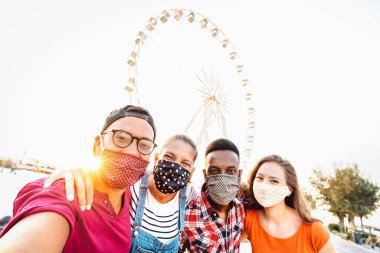 Yüz maskeleriyle korunan selfie çeken çok ırklı öğrenciler - Dönme dolapta güvenli bir şekilde eğlenen gençlerin olduğu yeni normal seyahat konsepti - eğimli açılı parlak güneş ışığı filtresi