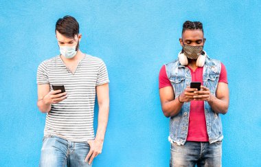 Yüz maskeli çok ırklı erkek arkadaşları cep telefonlu takip uygulaması kullanıyor - Sosyal medya ağlarındaki güncellemeleri izleyen genç milenyum insanları - parlak filtredeki yeni normal yaşam tarzı kavramı