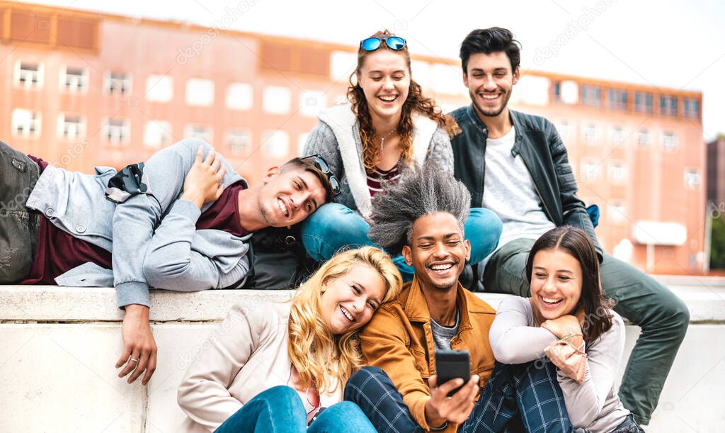 Happy millennial friends having fun with mobile phone after lockdown reopening - Joyful guys and girls spending fancy time together at university college break - Warm bright filter