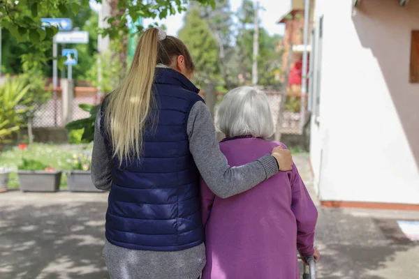 Cuidador joven caminando con la anciana en el jardín — Foto de Stock