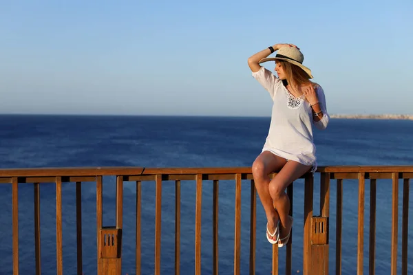 年轻漂亮的性感女人放松在泳衣和浅海滩礼服在露台上与蓝色大海和天空的背景。暑假概念. — 图库照片