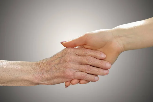 Руки молодых взрослых и пожилых женщин. Старшие и молодые держатся за руки снаружи. Концепция пожилых людей с легким фоном — стоковое фото