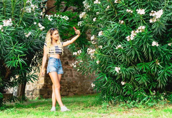 Joven hermosa chica con el pelo largo y rubio tomando una selfie en el teléfono inteligente en el parque . — Foto de Stock