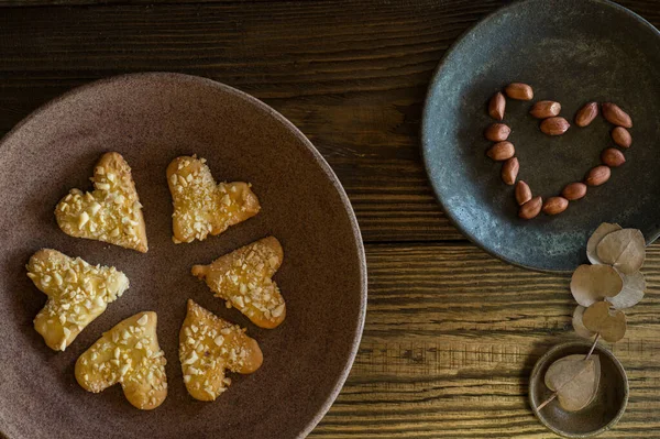 Composição de biscoitos de biscoito na forma de um coração, nozes dobradas na forma de um coração, galhos de eucalipto com folhas na forma de um coração em placas cerâmicas, vista superior . — Fotografia de Stock