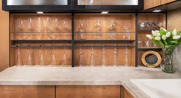 Un ramo de tulipanes blancos se encuentra sobre una mesa de mármol en el interior de una cocina moderna. Copas de vino de vidrio y vasos se colocan en estantes de madera . — Foto de Stock